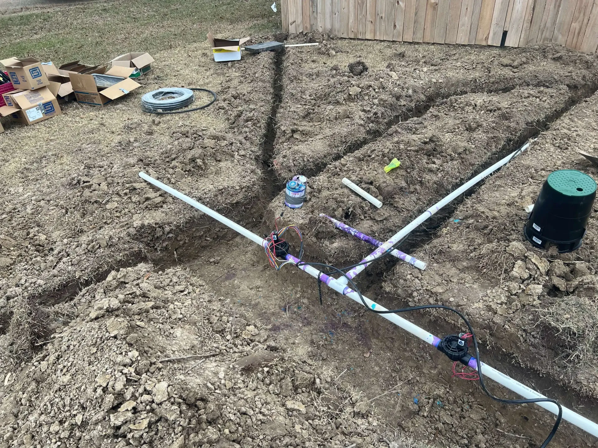 Irrigation system under construction with white PVC pipes in trenches, near a box, and a green valve.