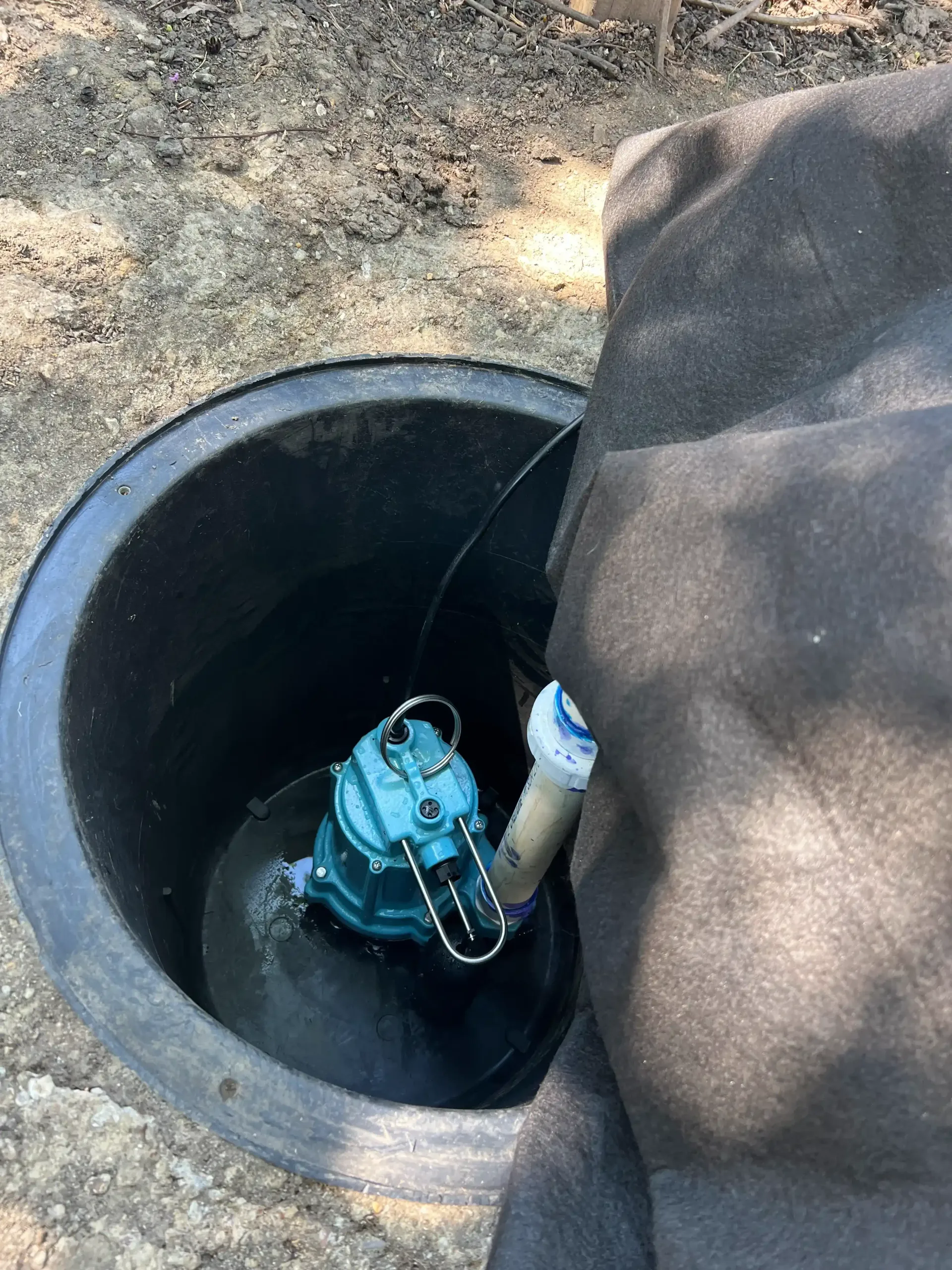 A submersible pump sits inside a dark tank, with a black covering.