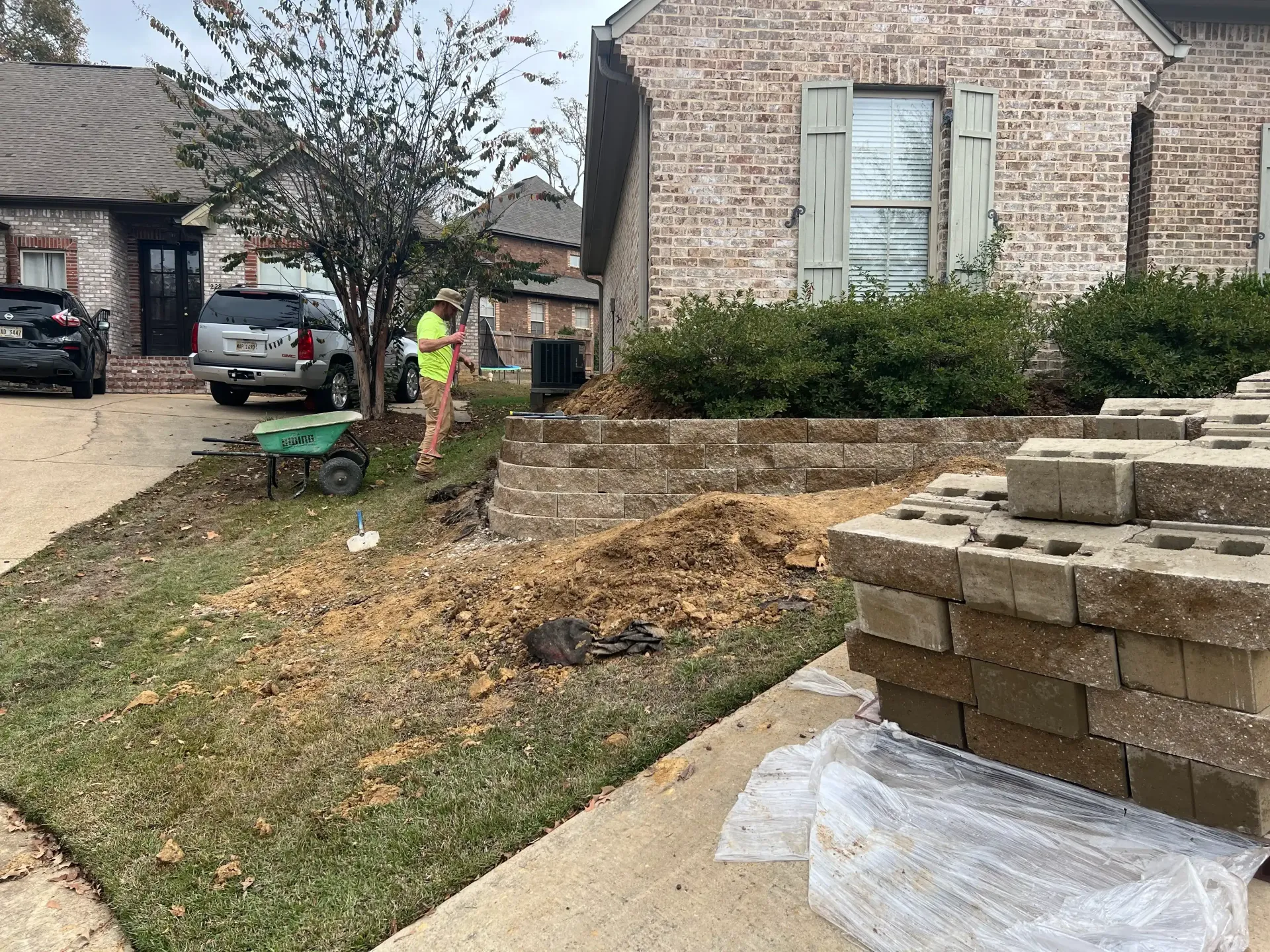 Person raking leaves in front yard; brick home, landscaping, and stacked pavers visible.