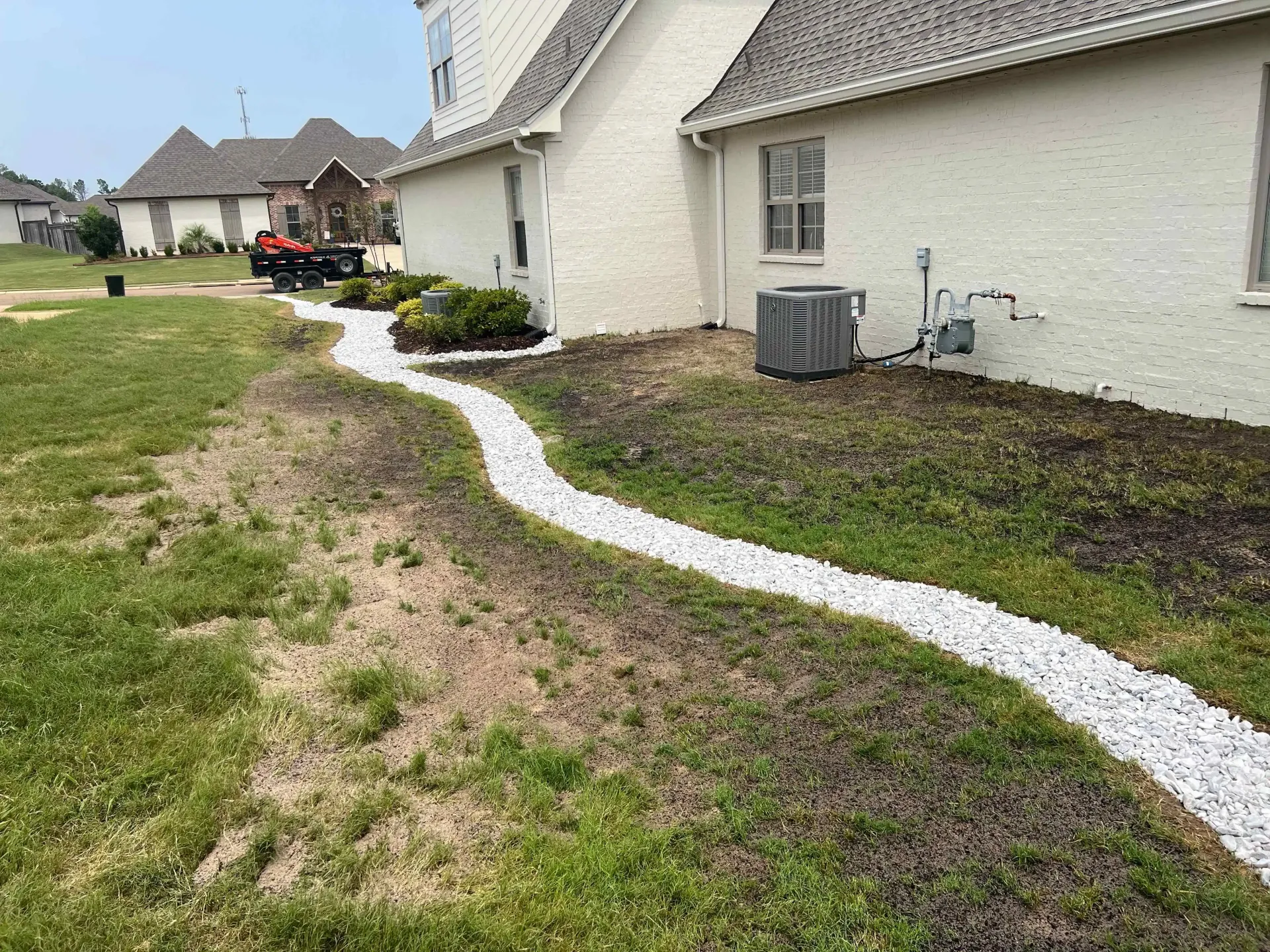 A white gravel drainage system winds along the side of a house, surrounded by grass.
