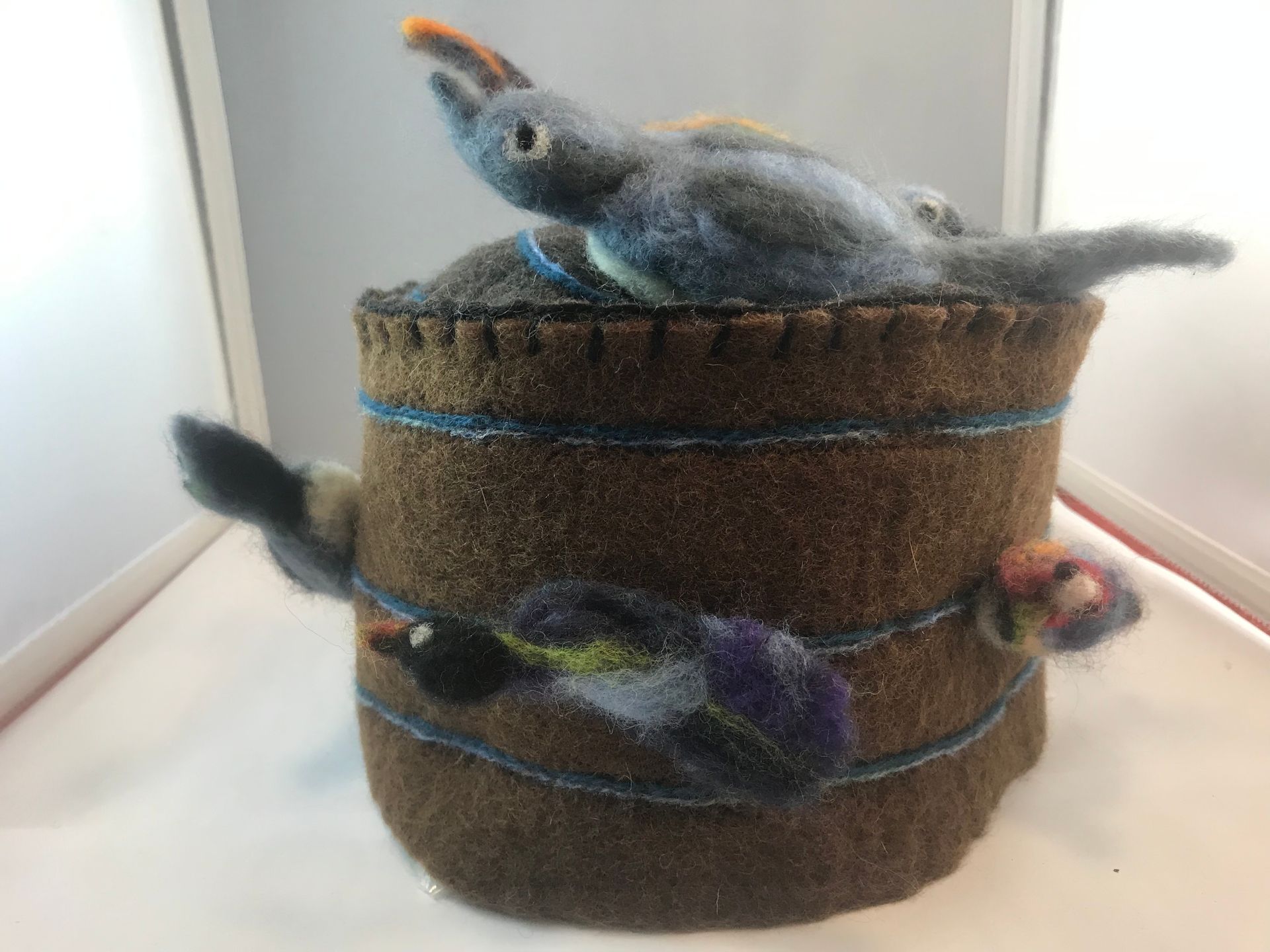 A needle felted bird is sitting on top of a barrel.
