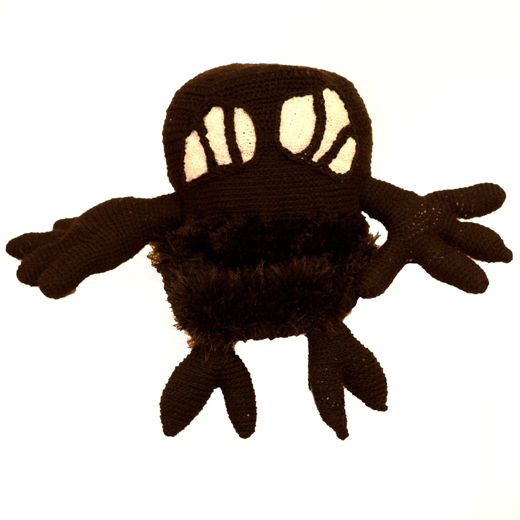 A stuffed black monster with white eyes and arms
