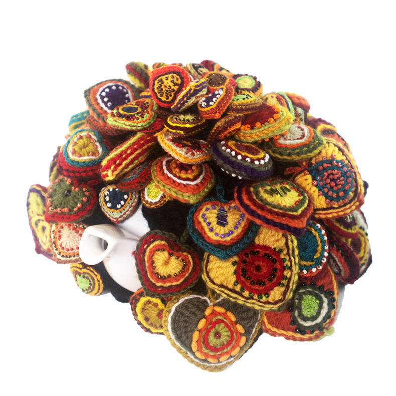 A white teapot sits in a pile of colorful crocheted hearts