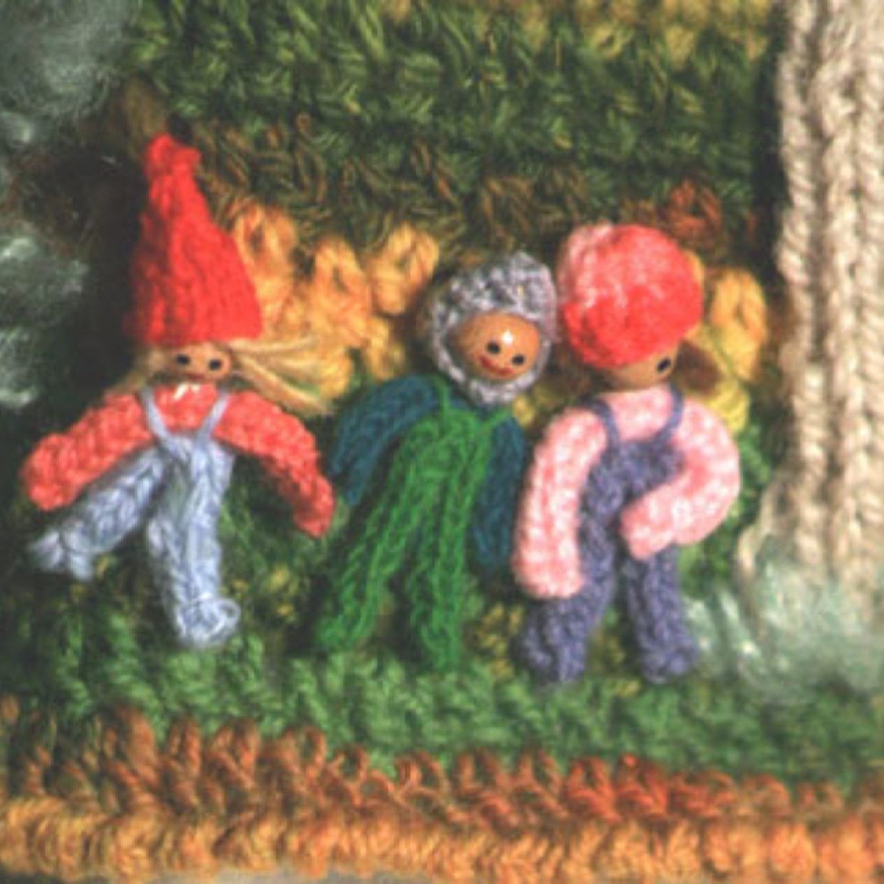 Three crocheted gnomes are standing next to each other on a blanket.