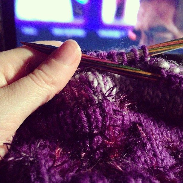A person is knitting with purple and white yarn