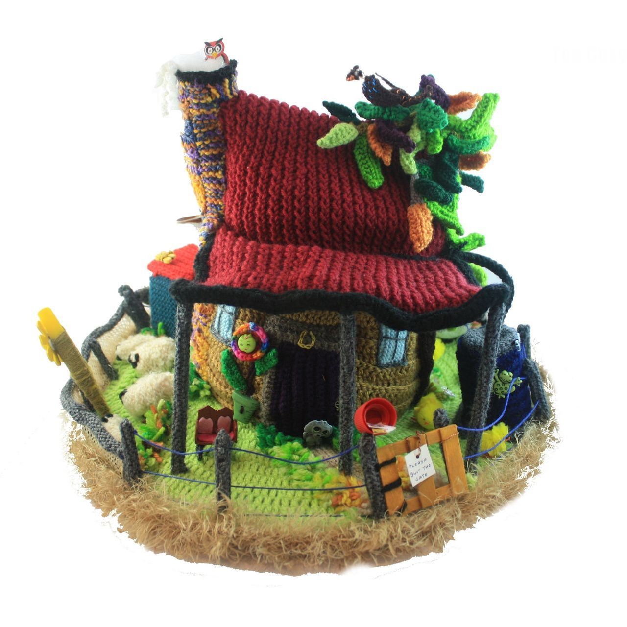 A knitted house with a red roof and a cat on top