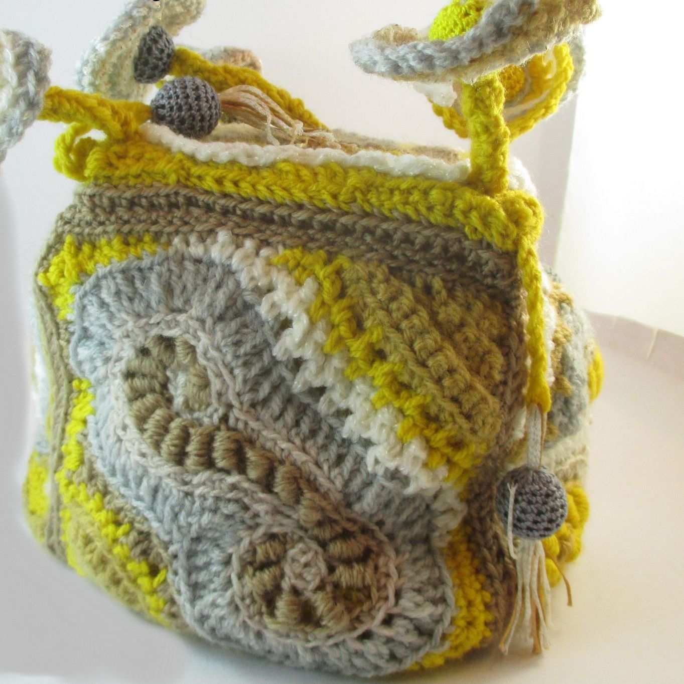 A yellow and grey crocheted purse with a tassel