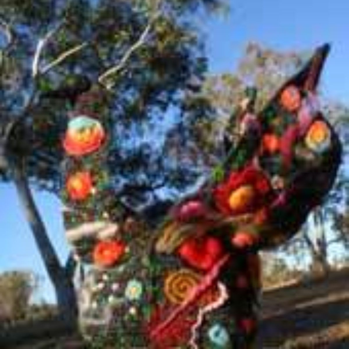 A statue of a dragon made of fruits and flowers is standing in front of a tree.