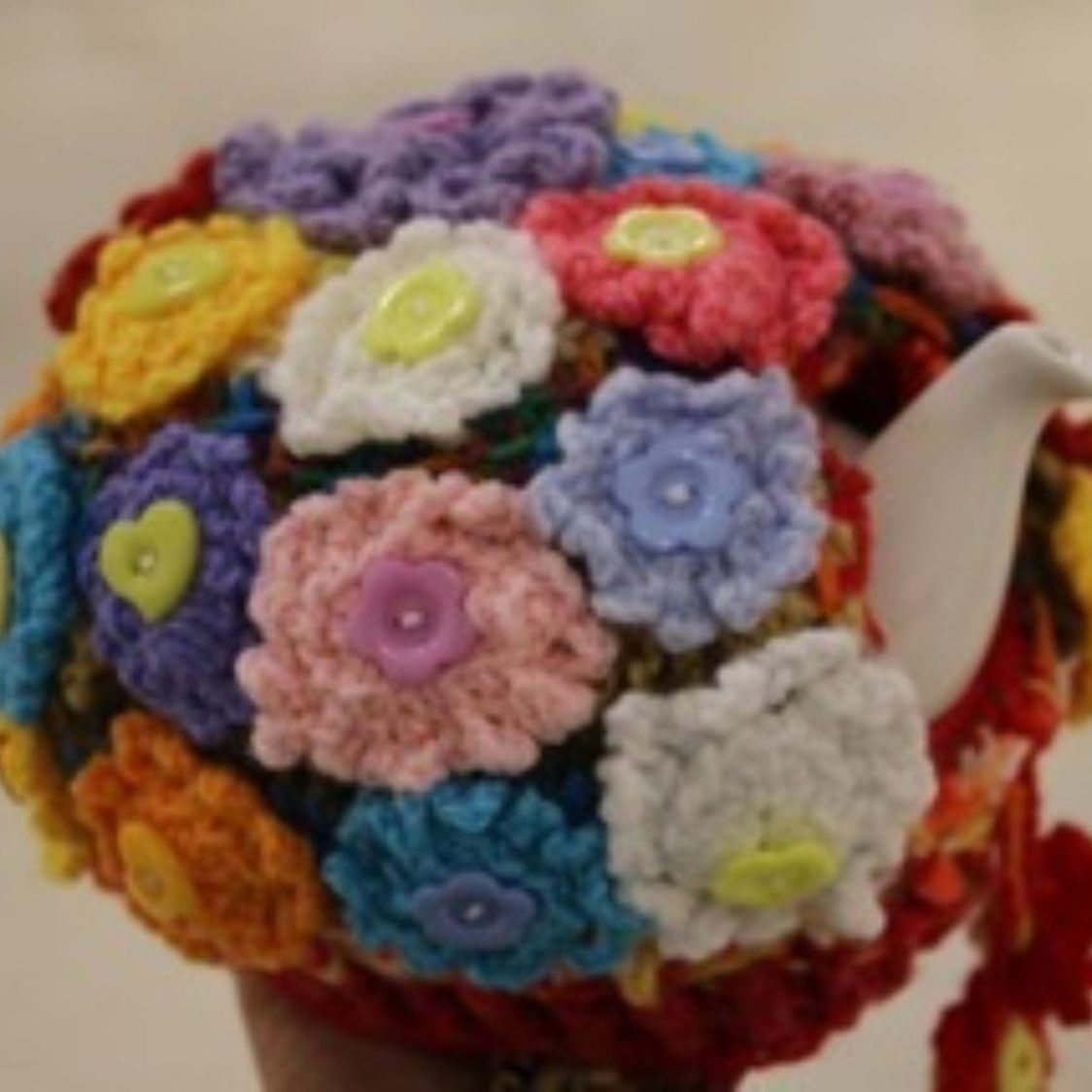 A person is holding a teapot decorated with crocheted flowers