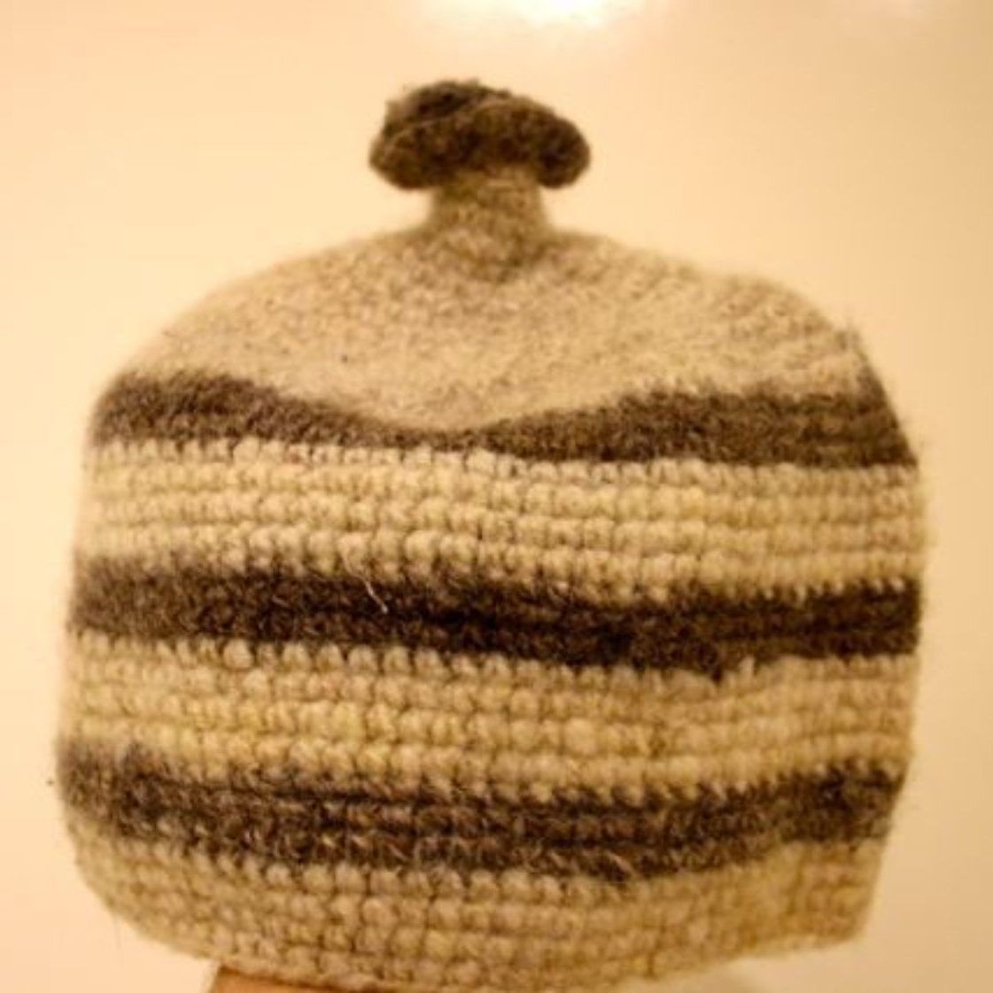 A person is holding a crocheted hat with a pom pom on top