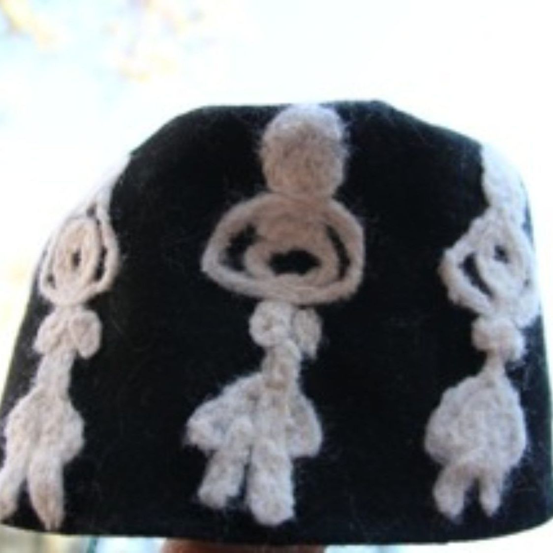 A person is holding a black hat with white crocheted designs on it
