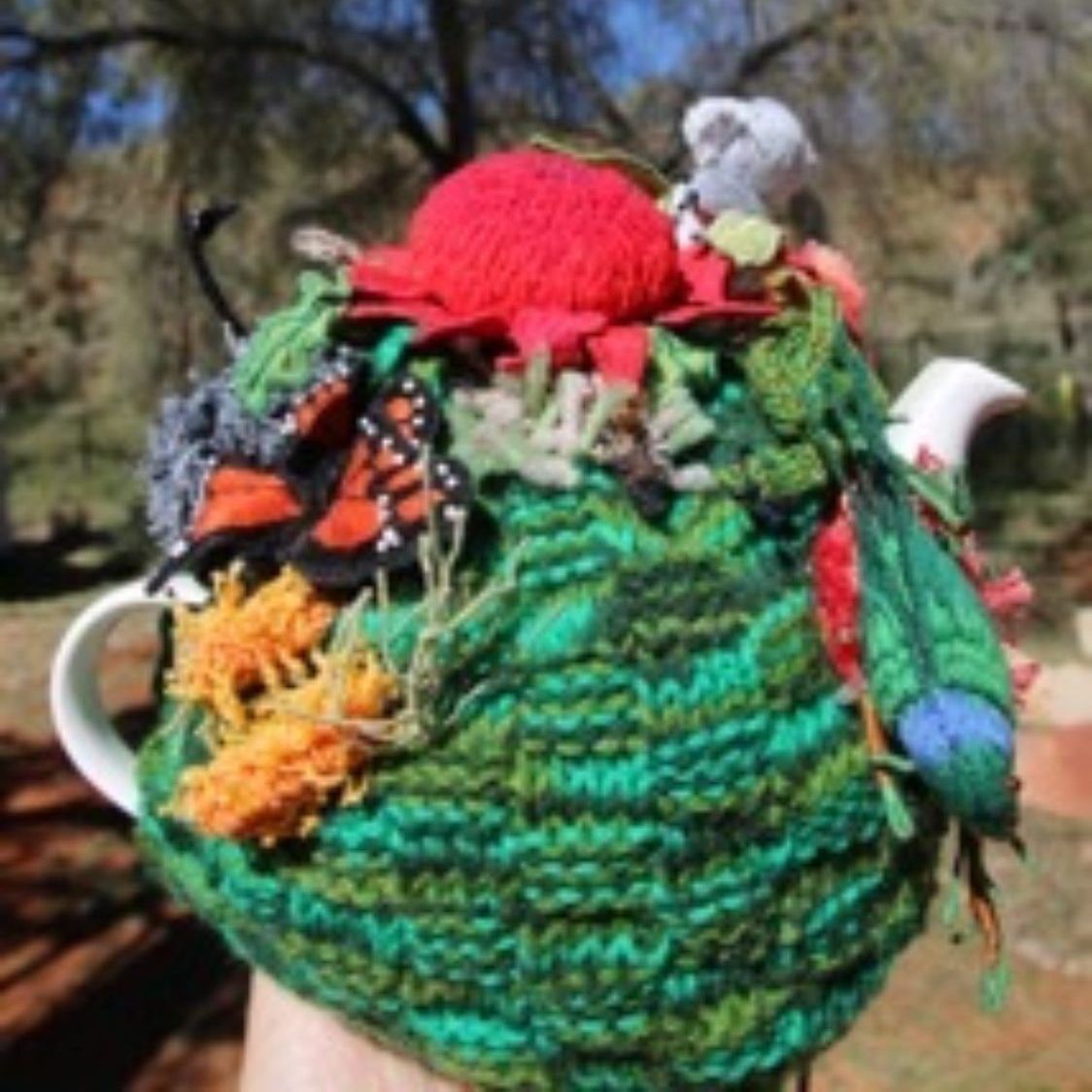 A person is holding a knitted teapot with butterflies and flowers on it