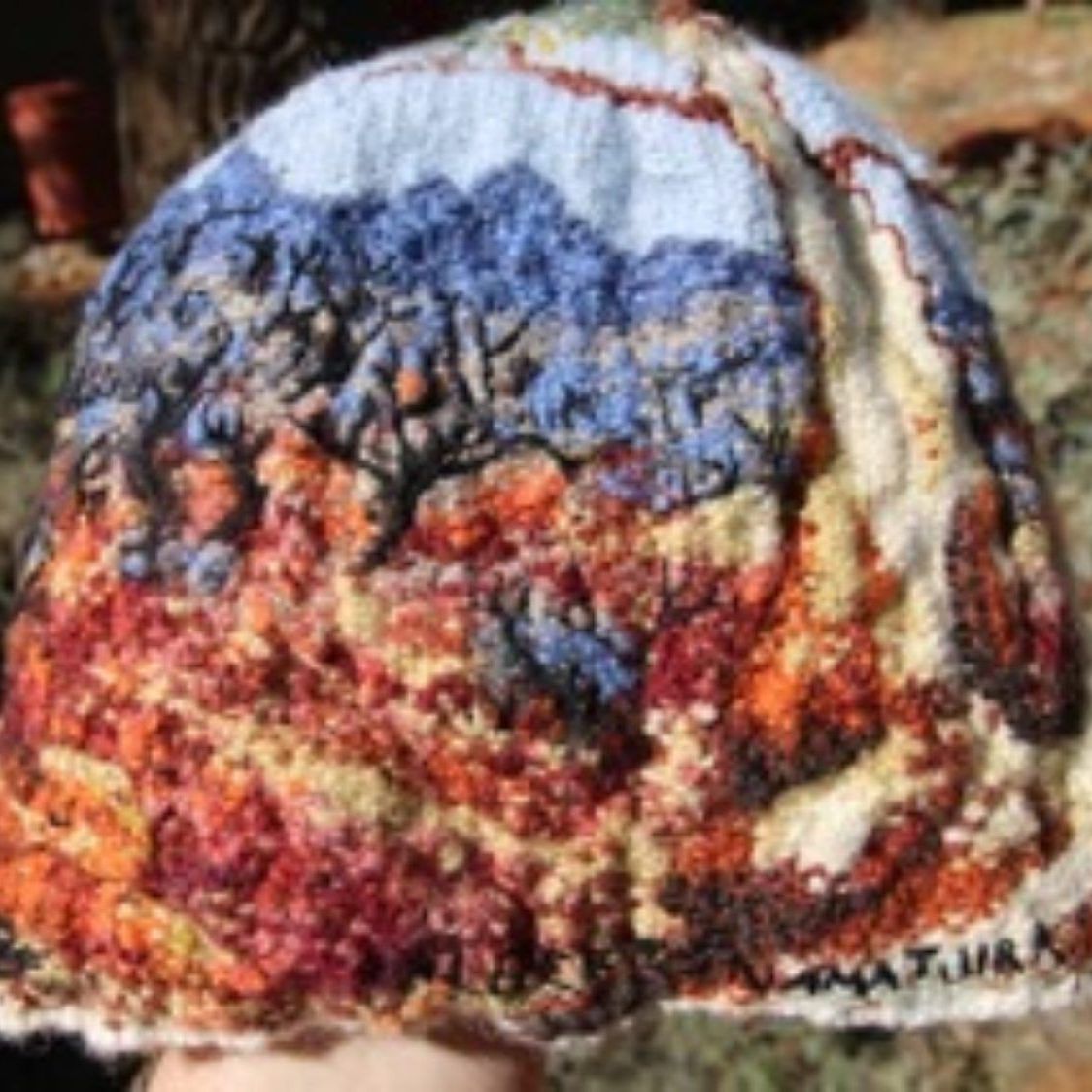 A person is holding a hat with a painting on it.