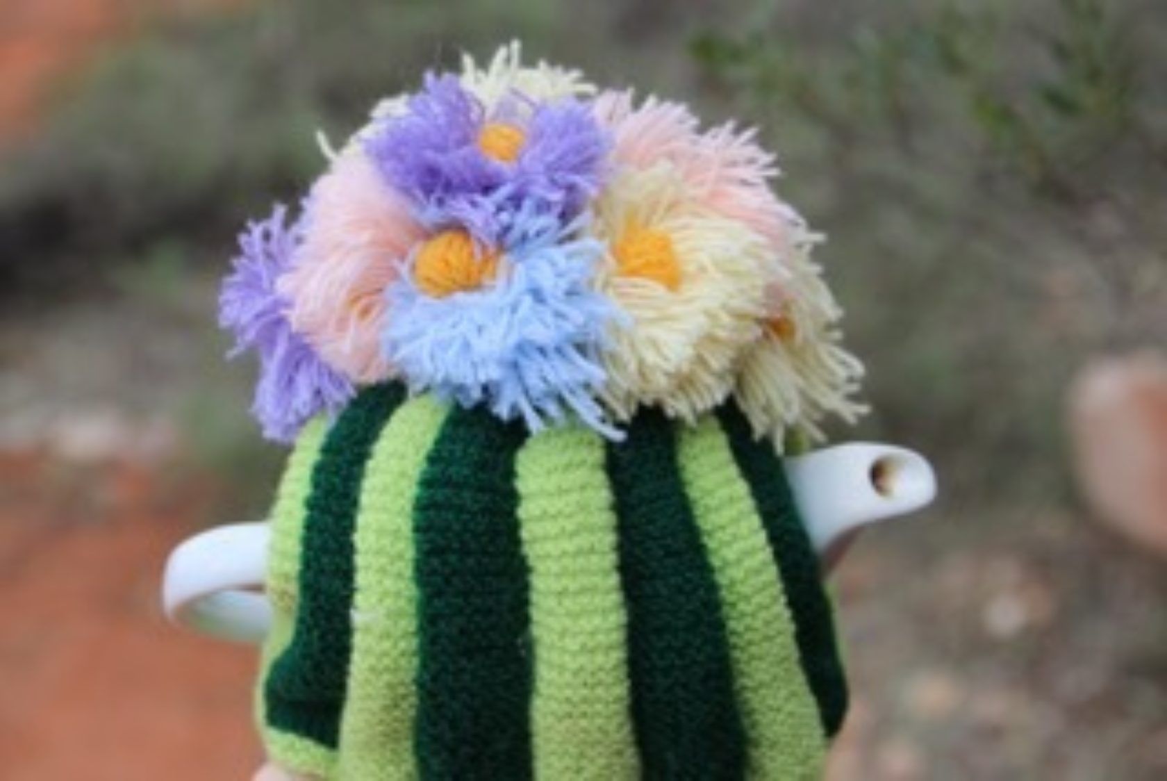 A person is holding a crocheted teapot with flowers on top of it.
