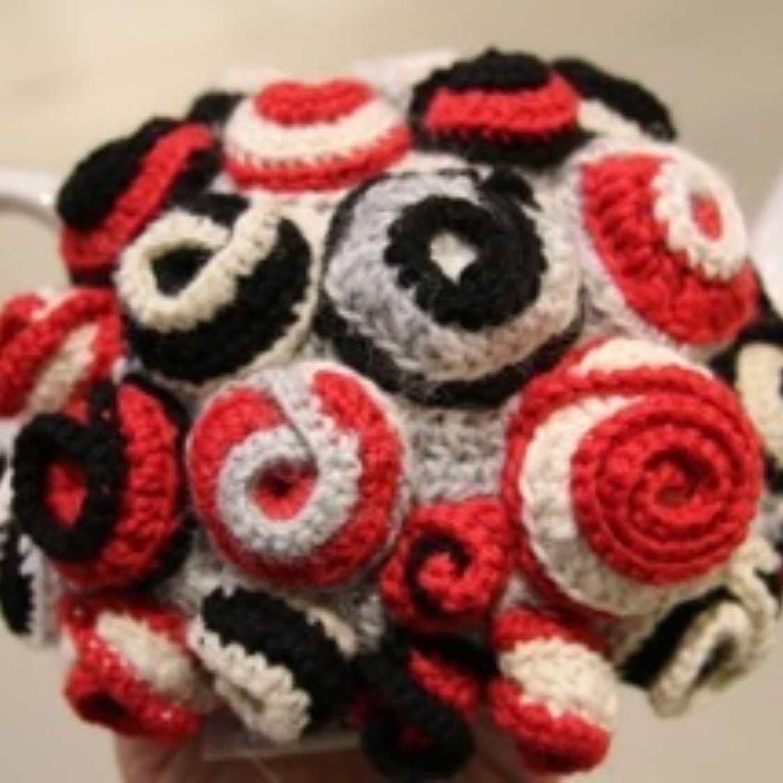 A person is holding a bunch of red white and black crocheted balls