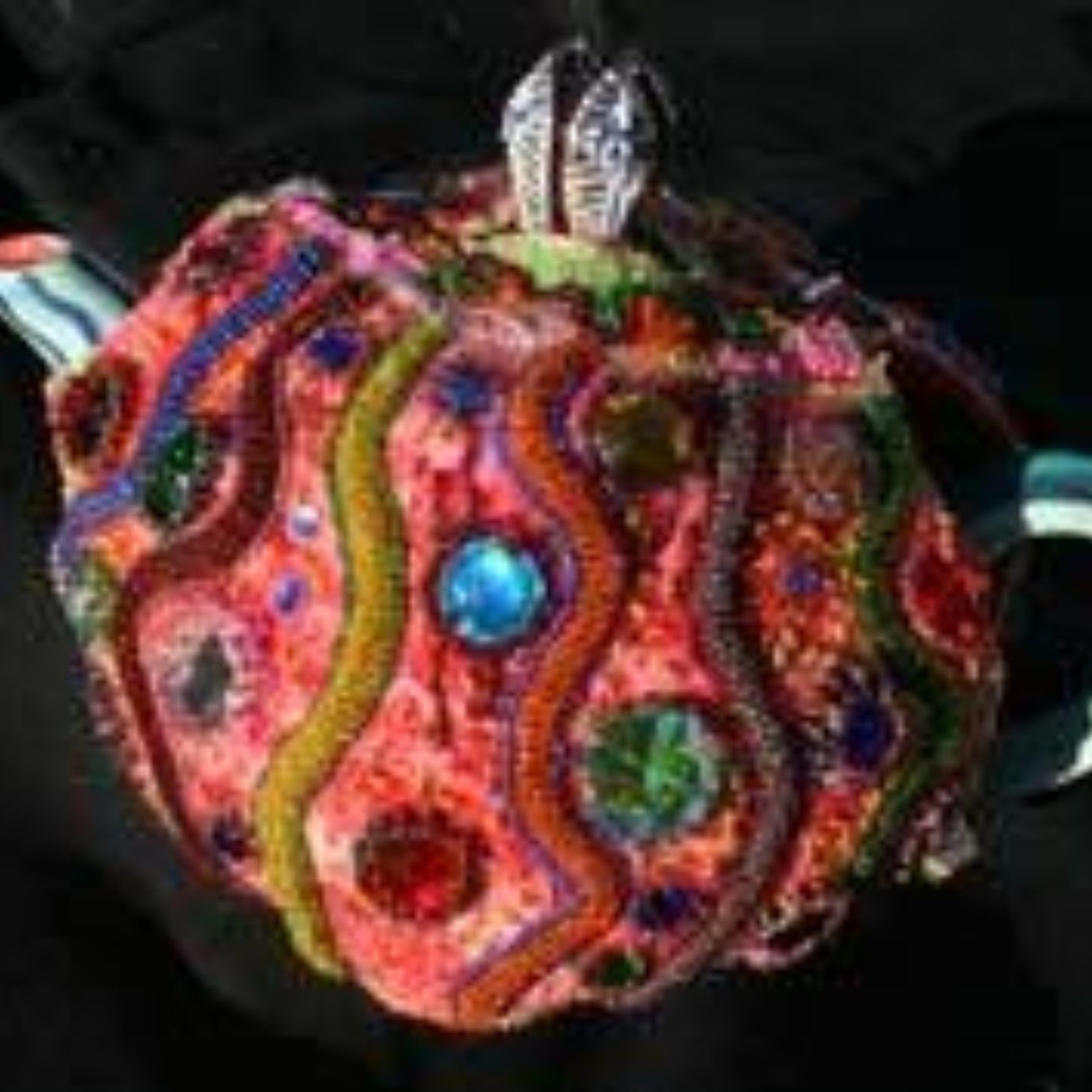 A close up of a colorful embroidered teapot on a black background.