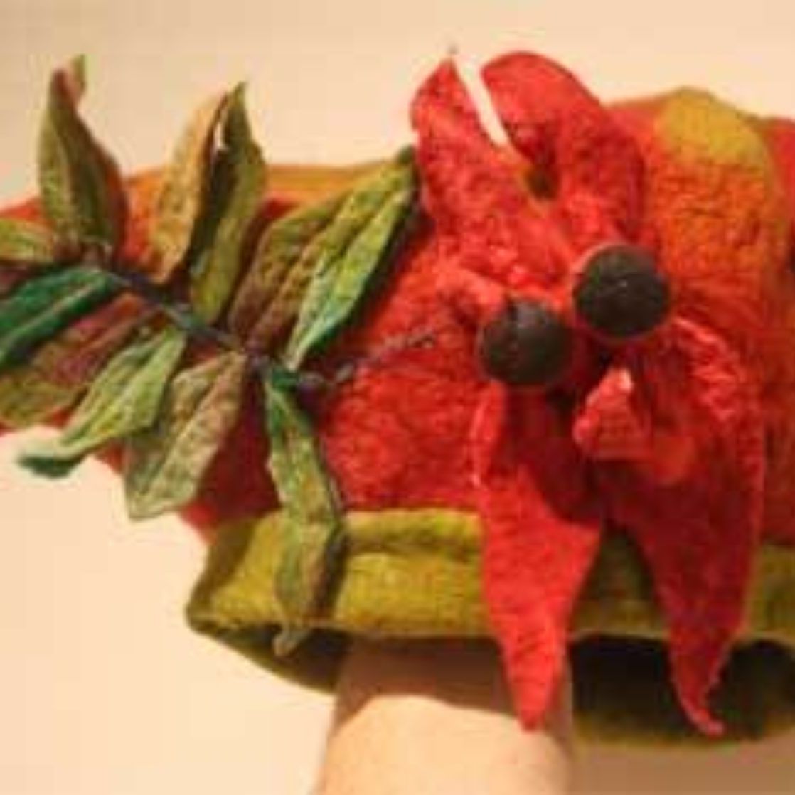 A person is holding a hat with a red flower and green leaves on it.