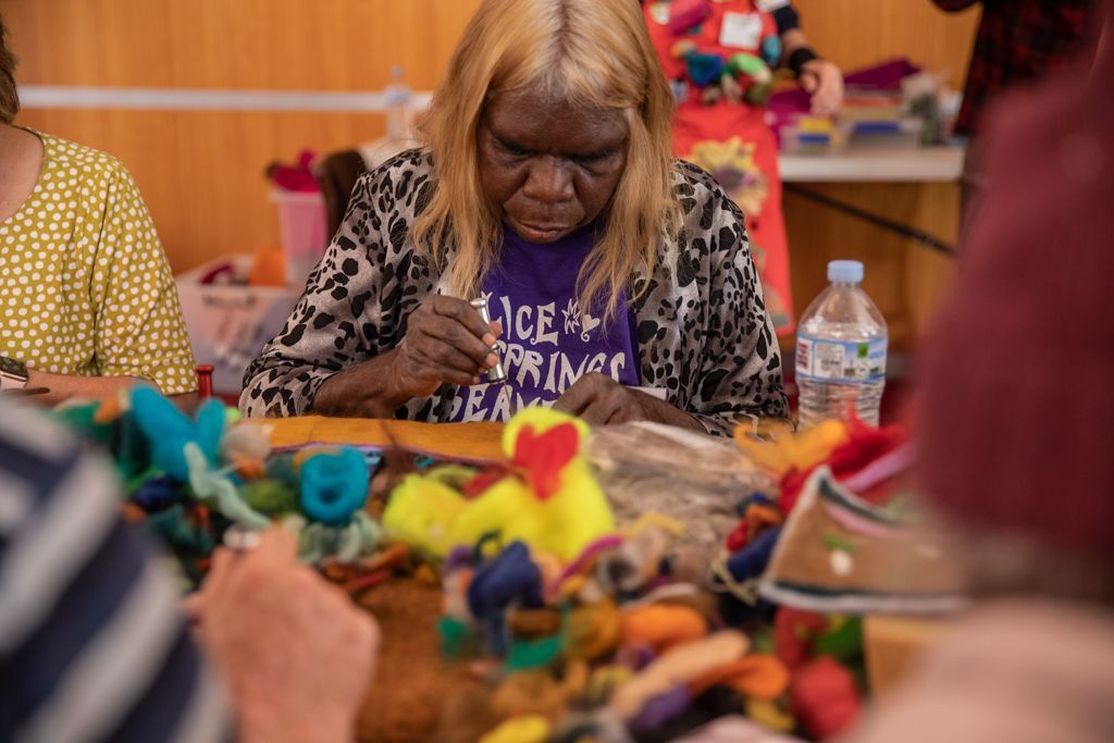 A woman is sitting at a table making a stuffed animal.