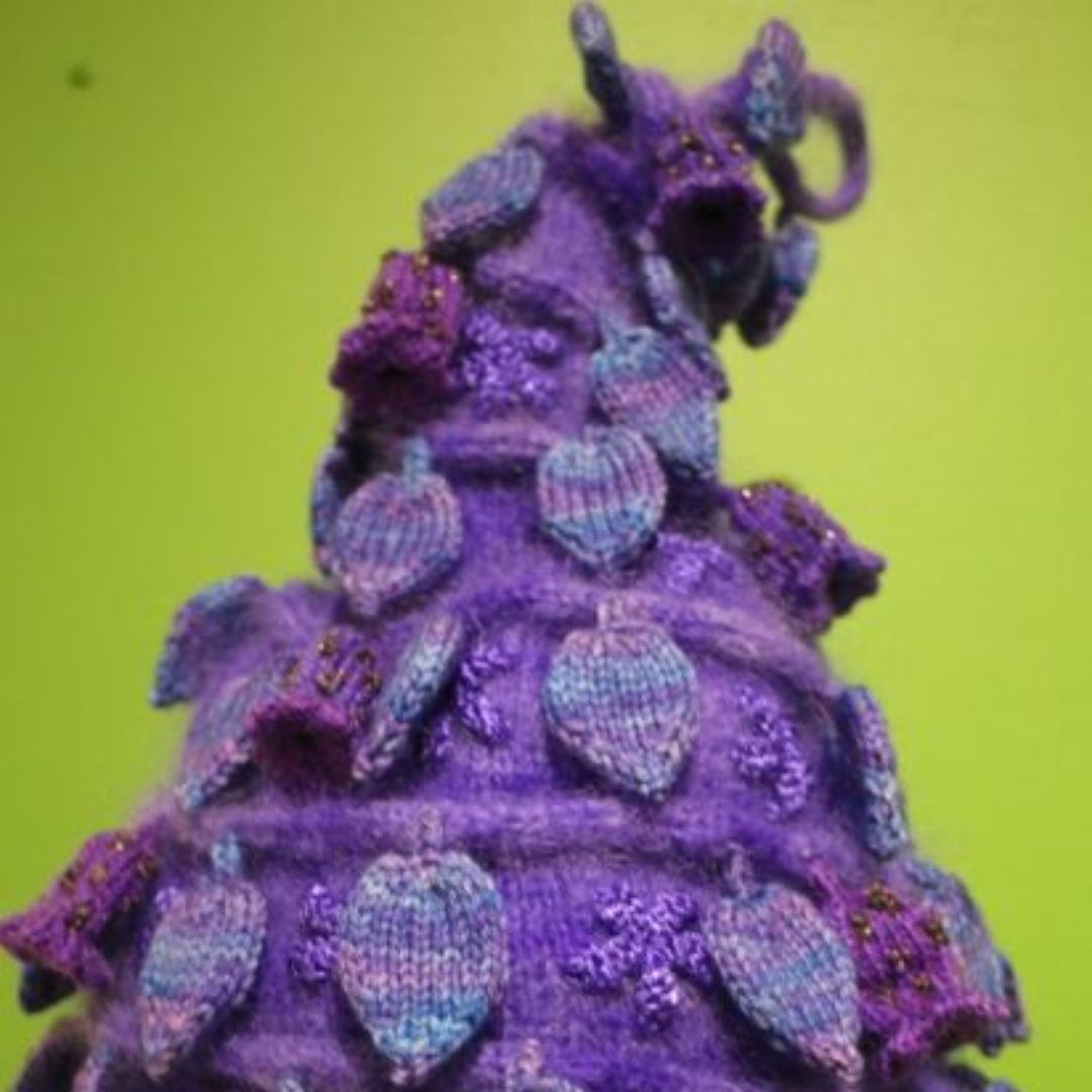 A close up of a purple knitted christmas tree on a green background.
