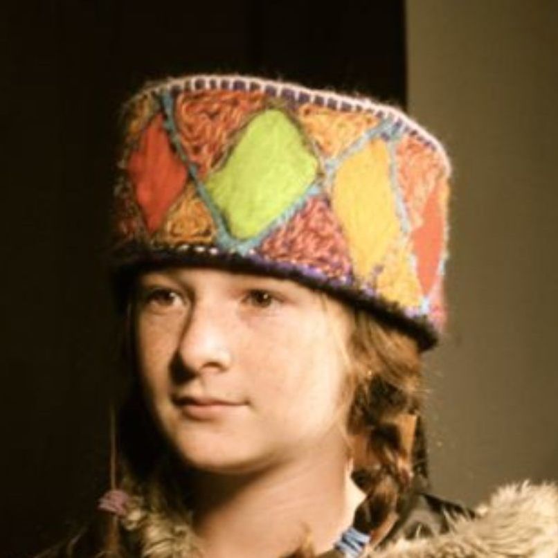 A young girl wearing a colorful hat and a fur coat