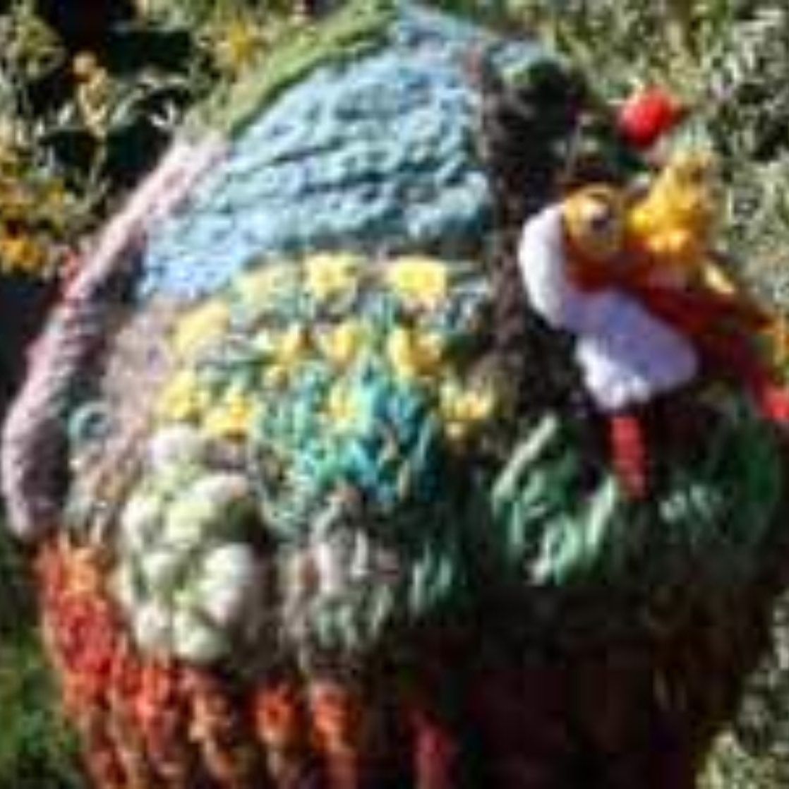 A knitted turkey with a yellow beak is sitting in the grass.