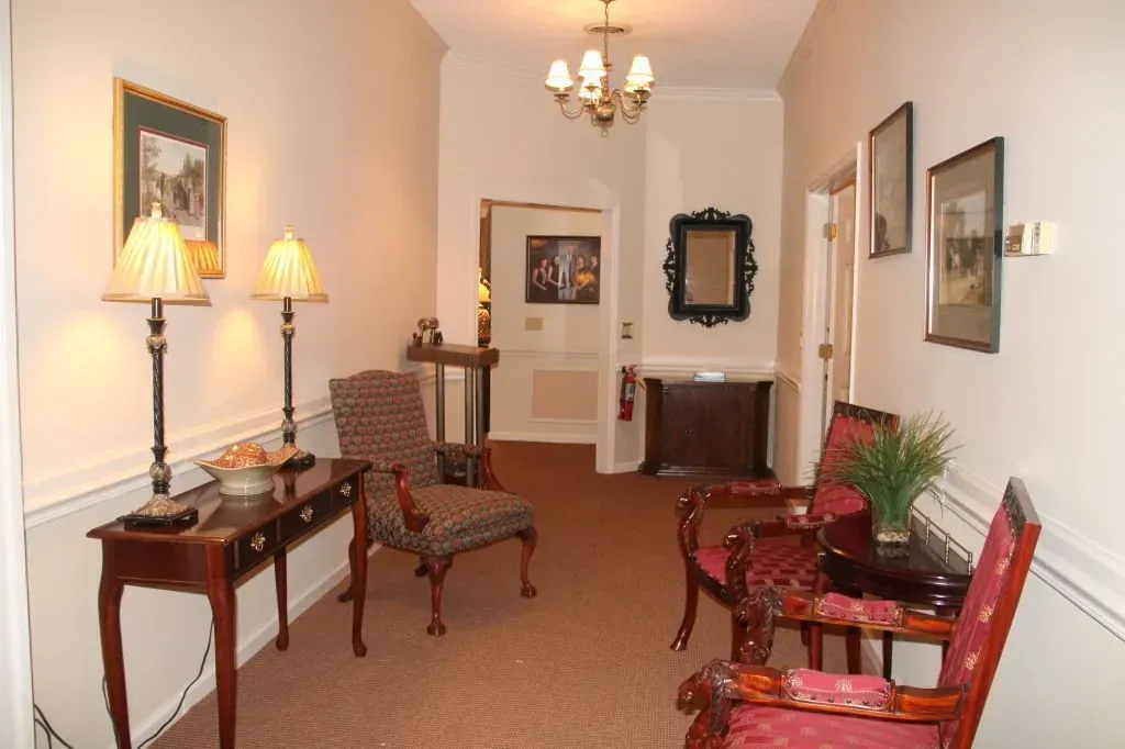 Hallway with antique furniture, lamps, artwork, and a chandelier. Carpeted floor, cream walls.