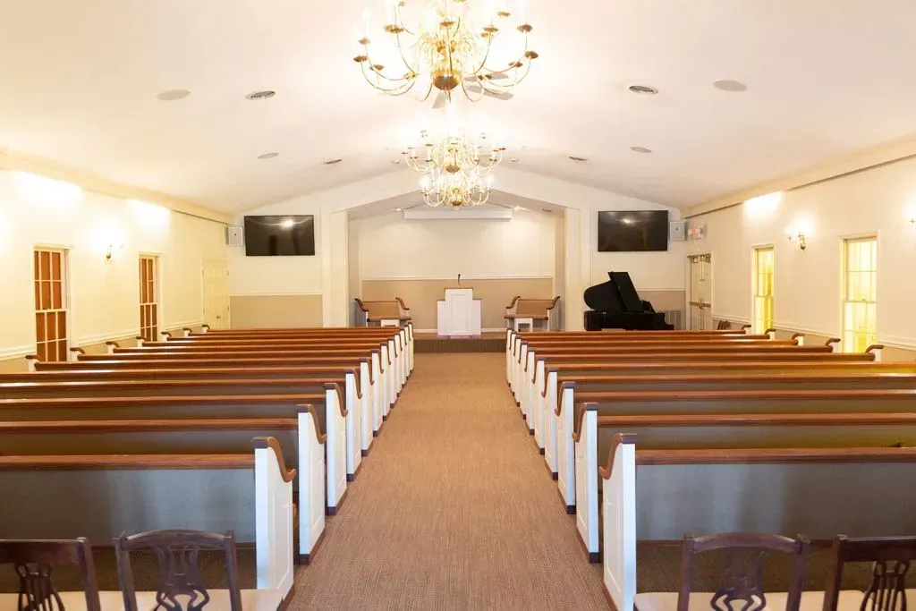 Interior of a chapel with rows of pews, a piano, and a stage with a podium.