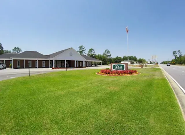Green lawn and sign in front of a brick building. American flag flies. Bright sunny day.