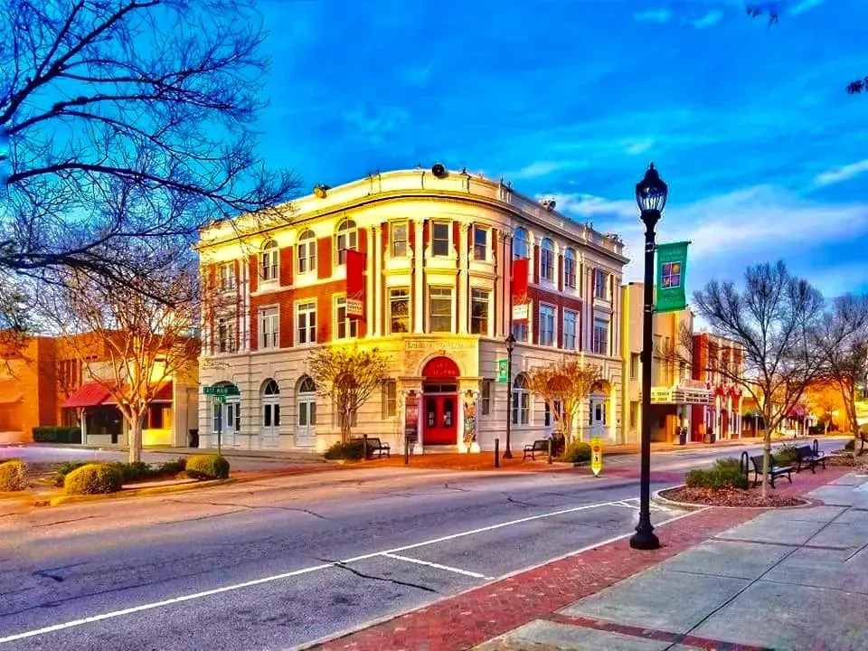 A three-story red-brick building with white columns and arches. A street and blue sky are in view.