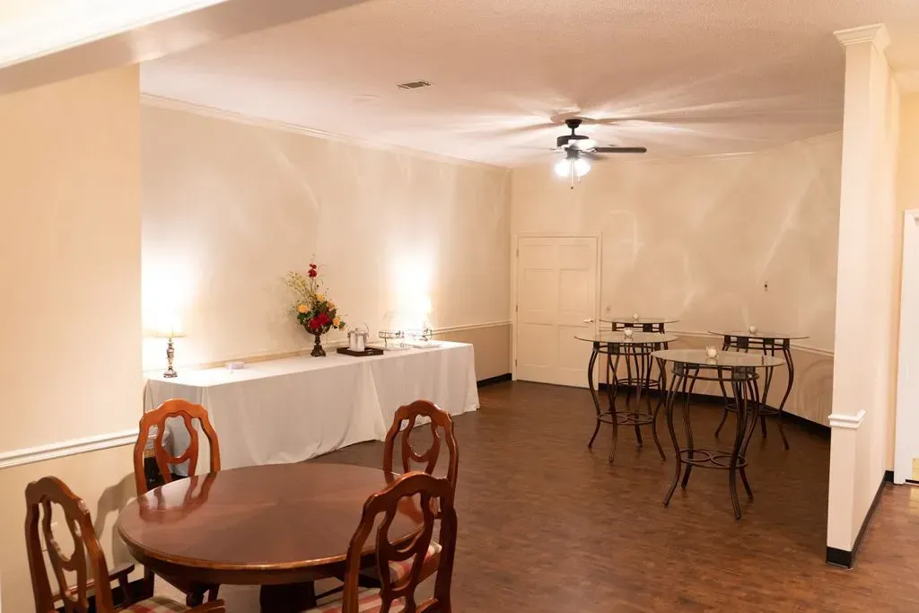 Empty event space with tables, chairs, and a buffet table.  Cream-colored walls, brown floor, ceiling fan.