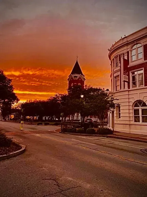 Sunset over a street with a red brick building, a clock tower, and trees. Orange sky.