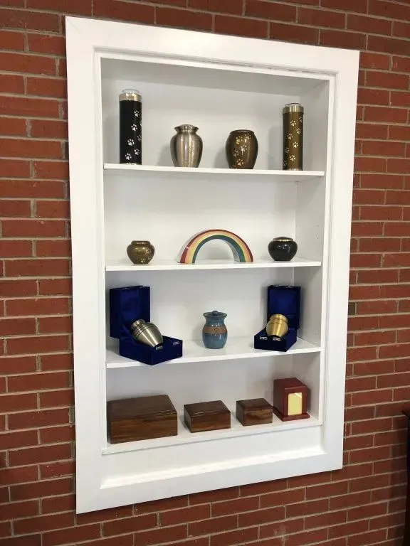 White shelf built into brick wall holding various cremation urns and mementos.