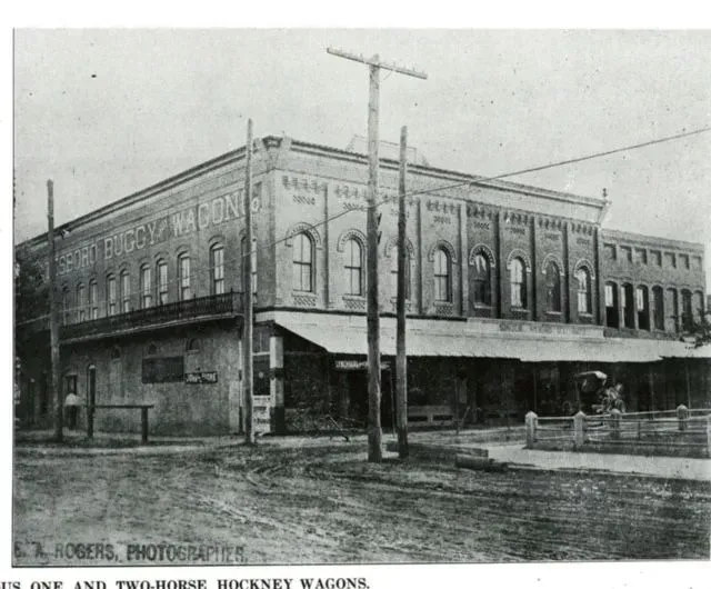 Two-story brick building with awning and two-horse buggy parked outside.