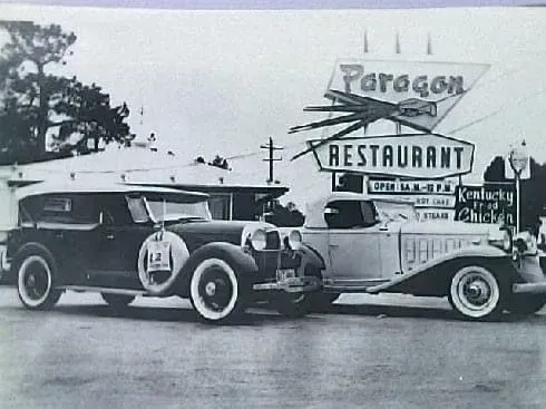 Two classic cars parked in front of the Paragon Restaurant sign.