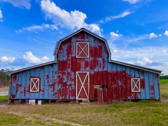 Red and blue weathered barn with white accents against a blue sky with clouds.