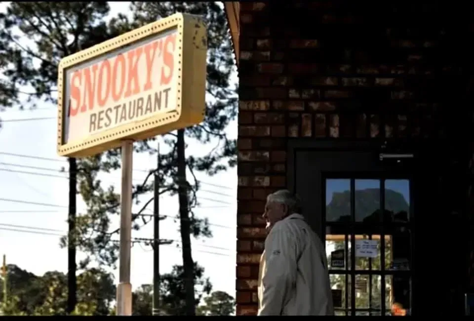 Sign for Snooky's Restaurant, exterior view of brick building, elderly man stands near door.