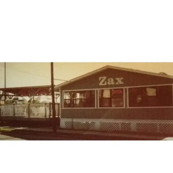 Zax restaurant exterior with a covered patio, featuring a sign and windows.