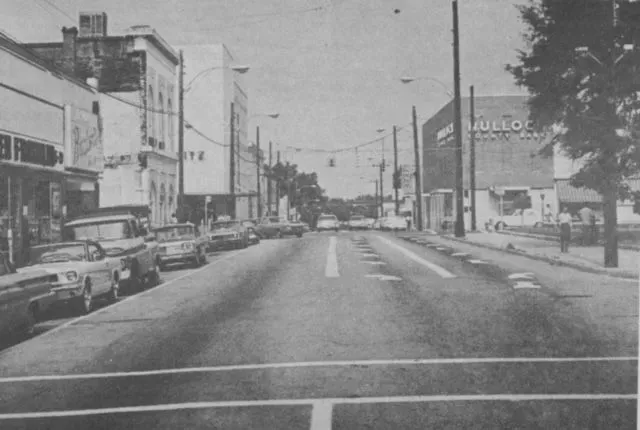 Street lined with cars, buildings, and a large sign.