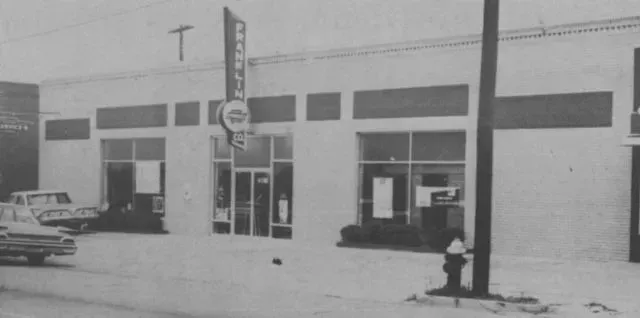 Exterior of a building with a tall sign; a car parked in front.