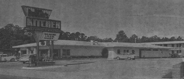 Black and white photo of a motel, with a large sign in front.