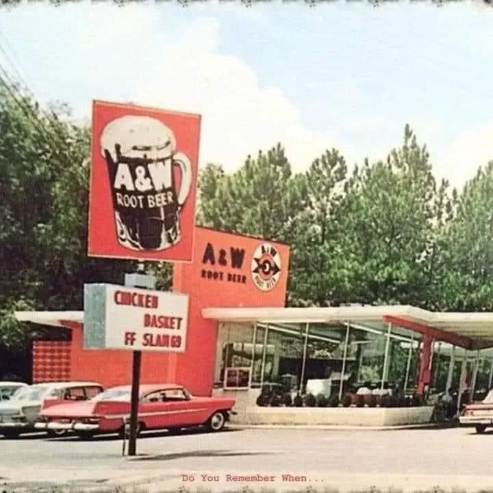 Vintage A&W Root Beer restaurant with red exterior, cars parked out front, and a large sign.