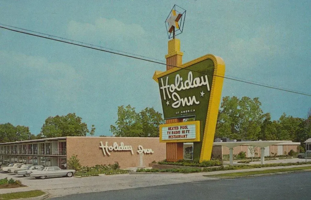 Vintage Holiday Inn motel with large neon sign and classic cars parked in front.