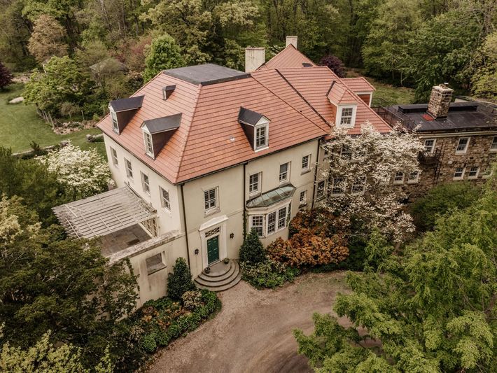 An aerial view of a large white house with a red tile roof surrounded by trees.