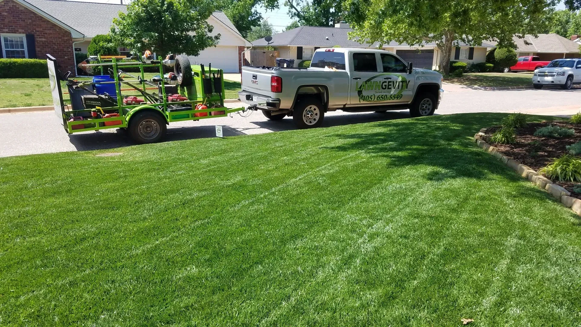 A truck towing lawn care equipment on a green lawn in a suburban neighborhood.