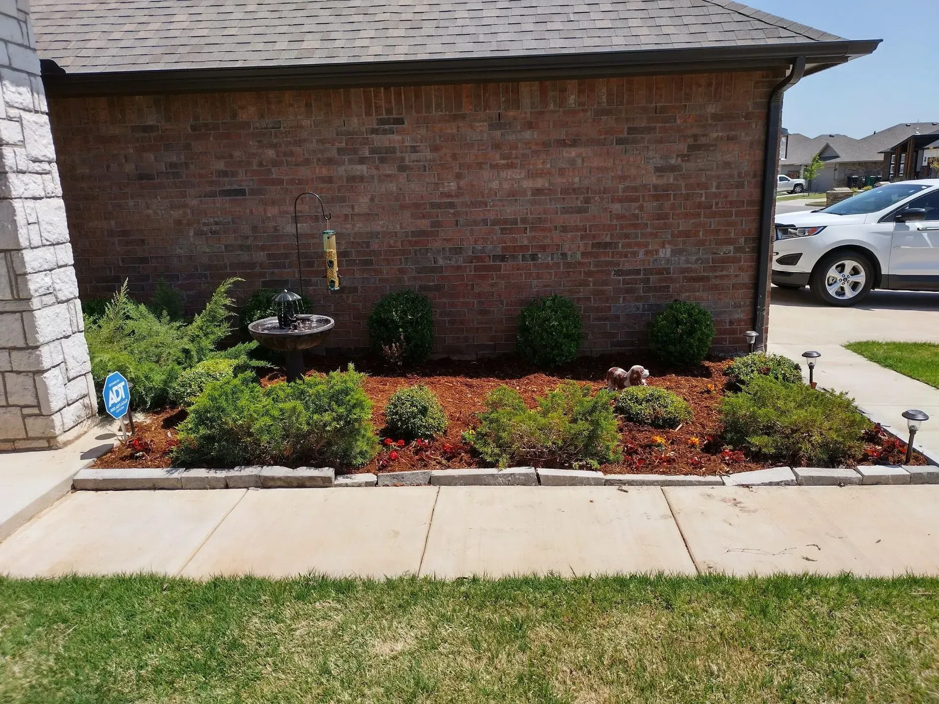 Brick building with flower bed containing green shrubs and red mulch.