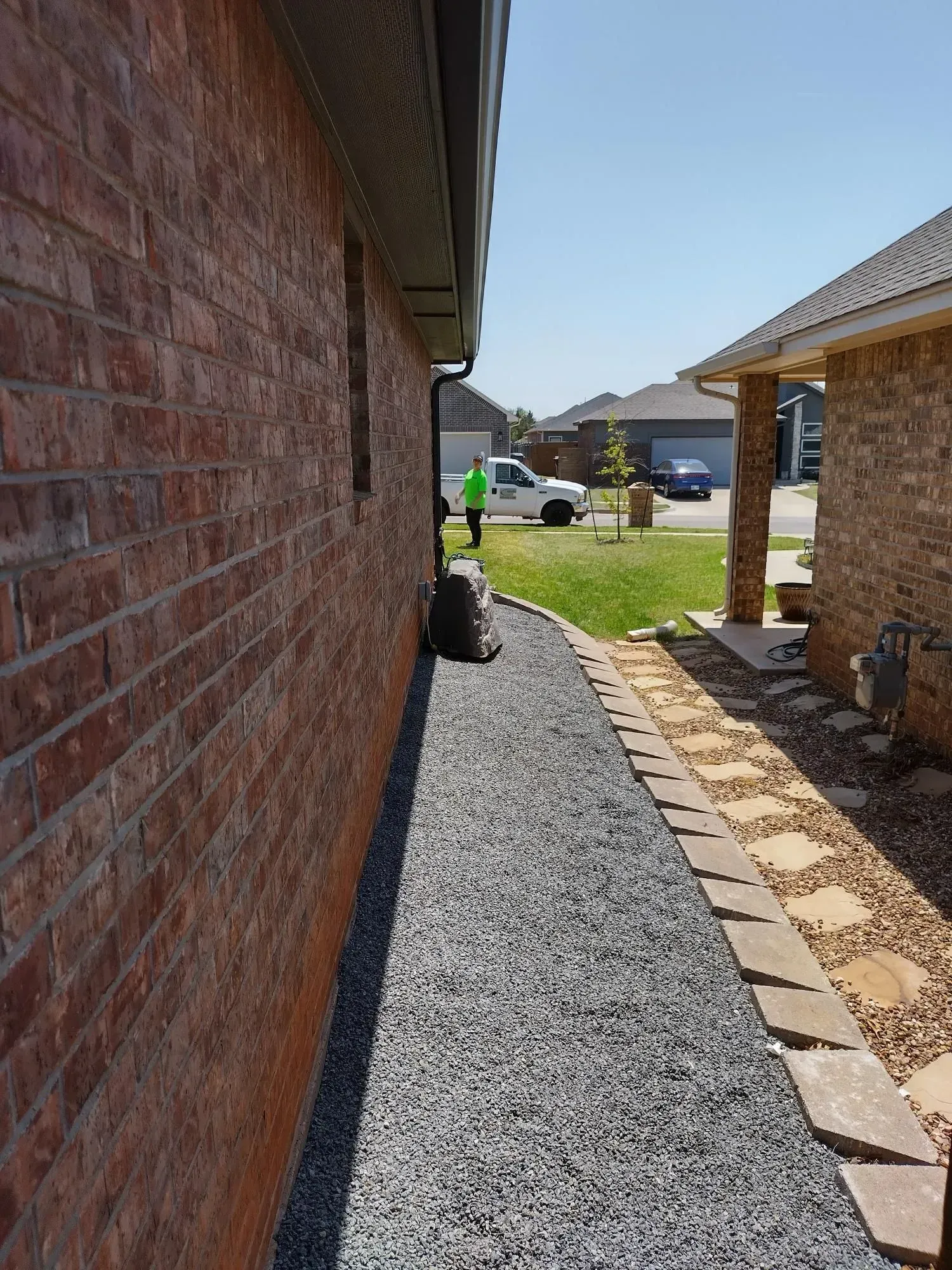 A gravel pathway between brick buildings. A person stands near a white van on the lawn.