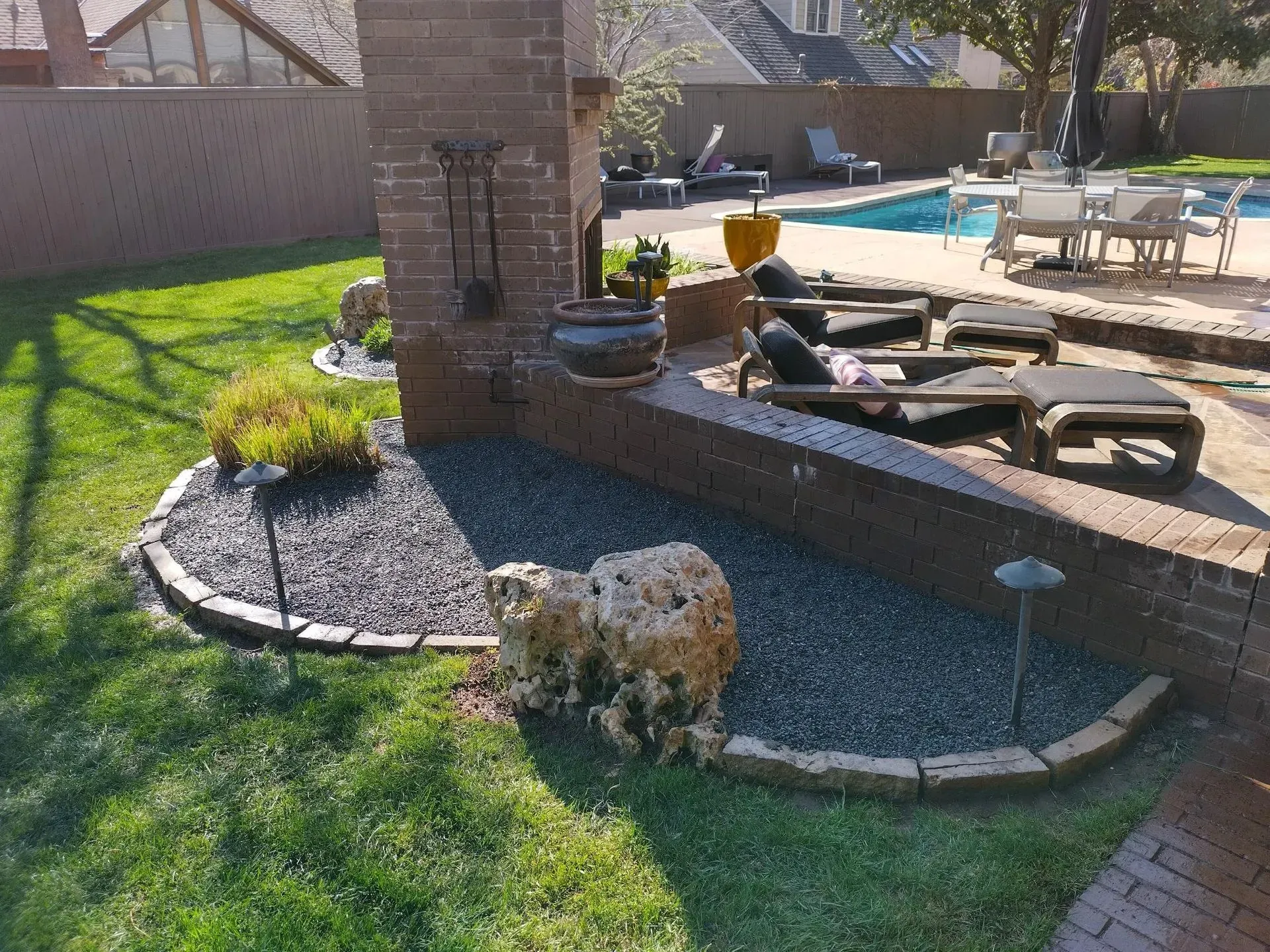 Backyard with brick structure, pool, and seating areas; green grass and dark gravel landscaping.