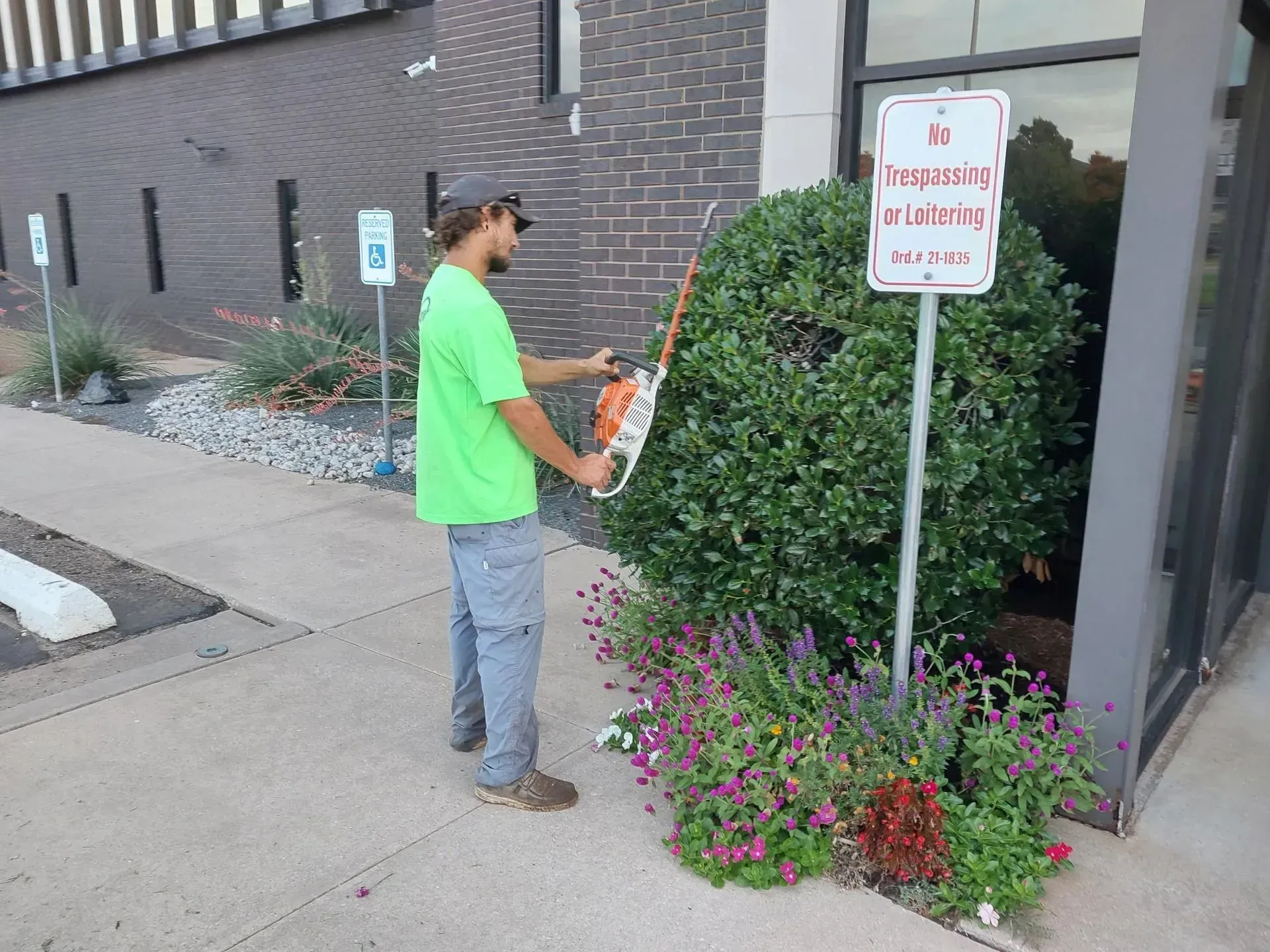 Man trimming a bush near a sign that says 