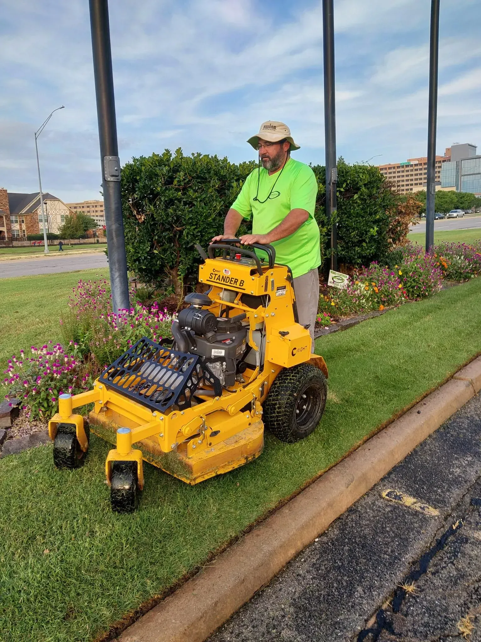 Person mowing a green grassy area with a yellow lawnmower along a curb.