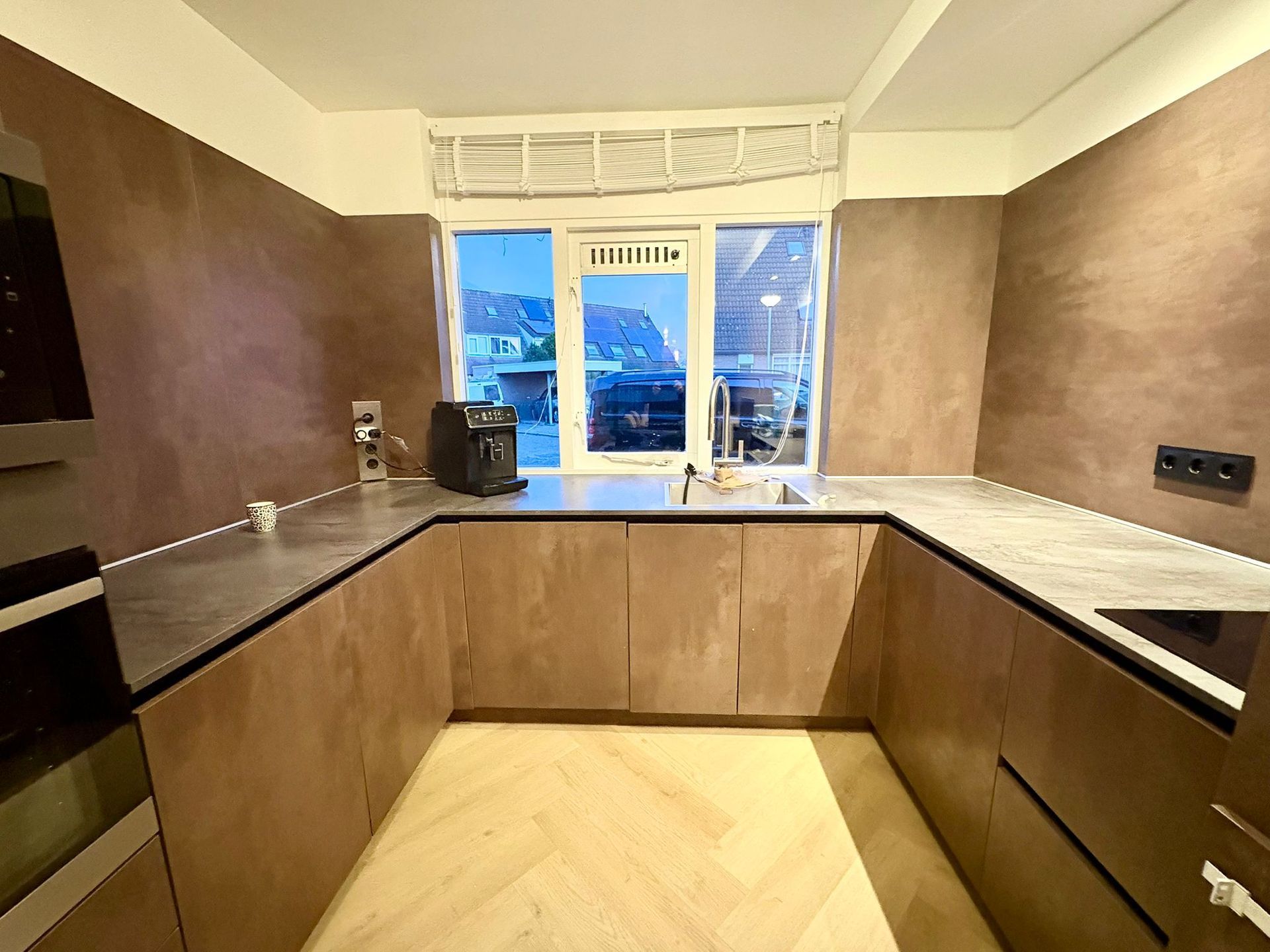 U-vormige keuken met bruine kasten, donkere werkbladen en een raam met uitzicht op de stad.